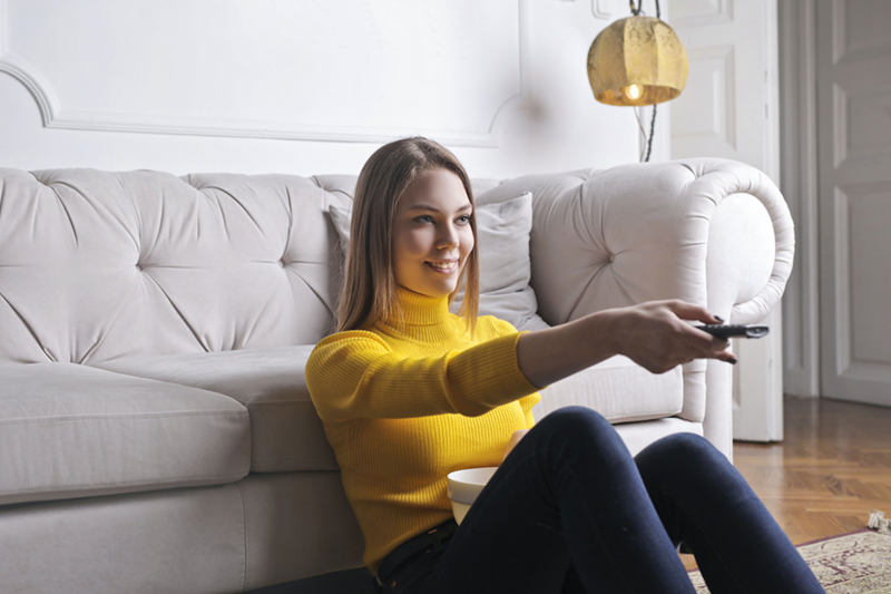 woman leaning on a couch while pointing out a remote